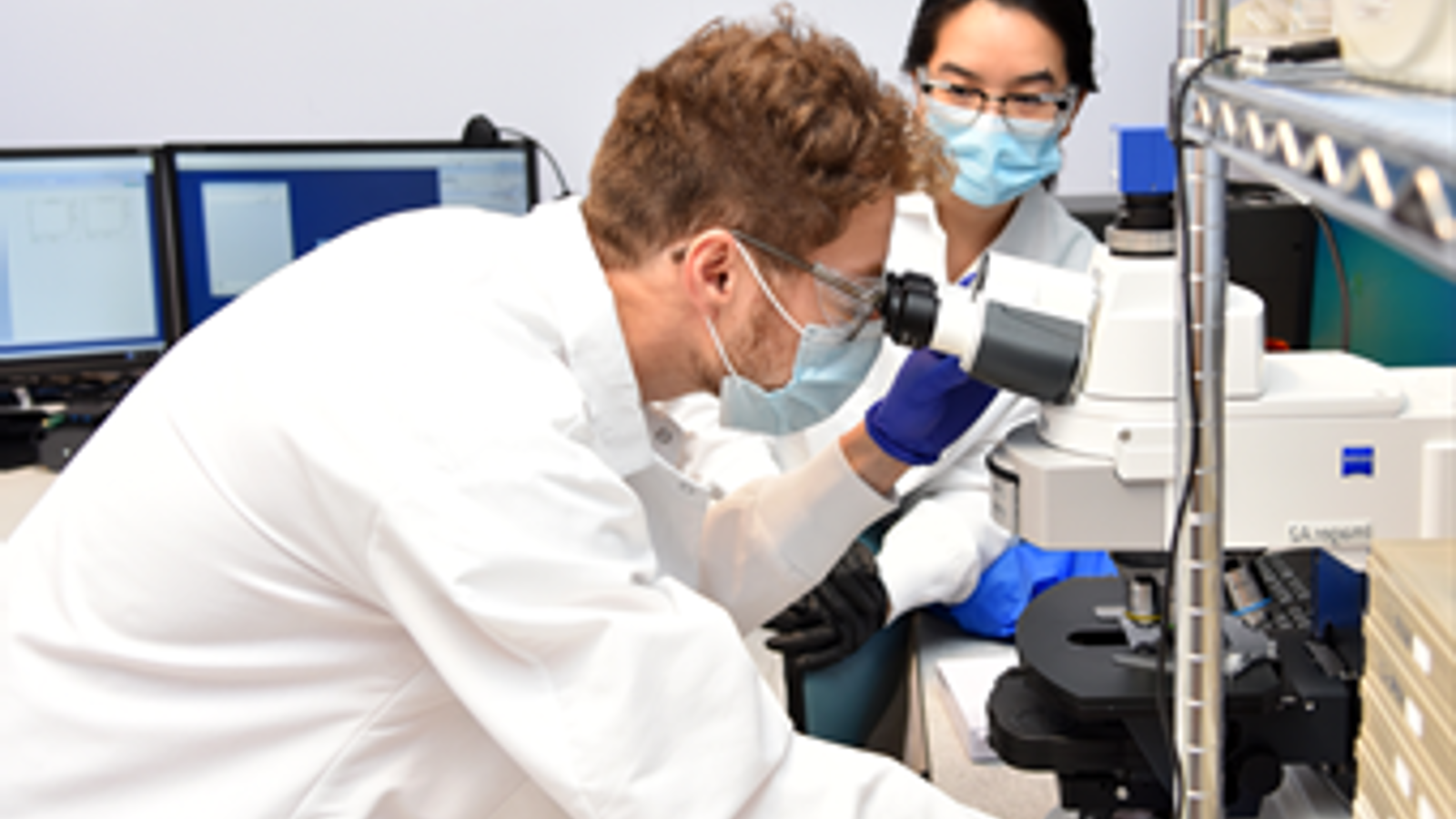 a man and woman in white coats looking through a microscope