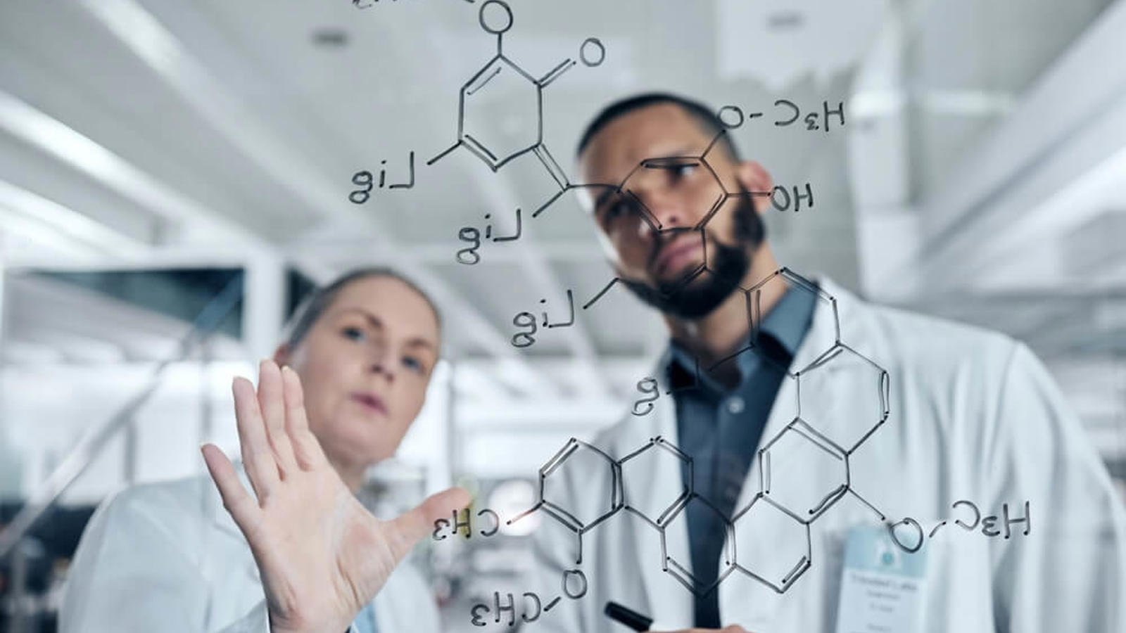 un homme et une femme en blouse de laboratoire écrivant sur un panneau de verre